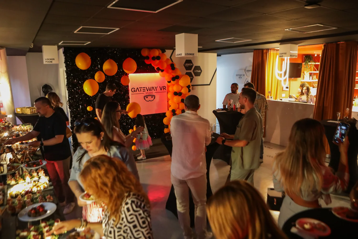 Aceeași sală în configurație de eveniment: mese înalte de cocktail, bufet și fundal foto, cu barul de cafea în dreapta.